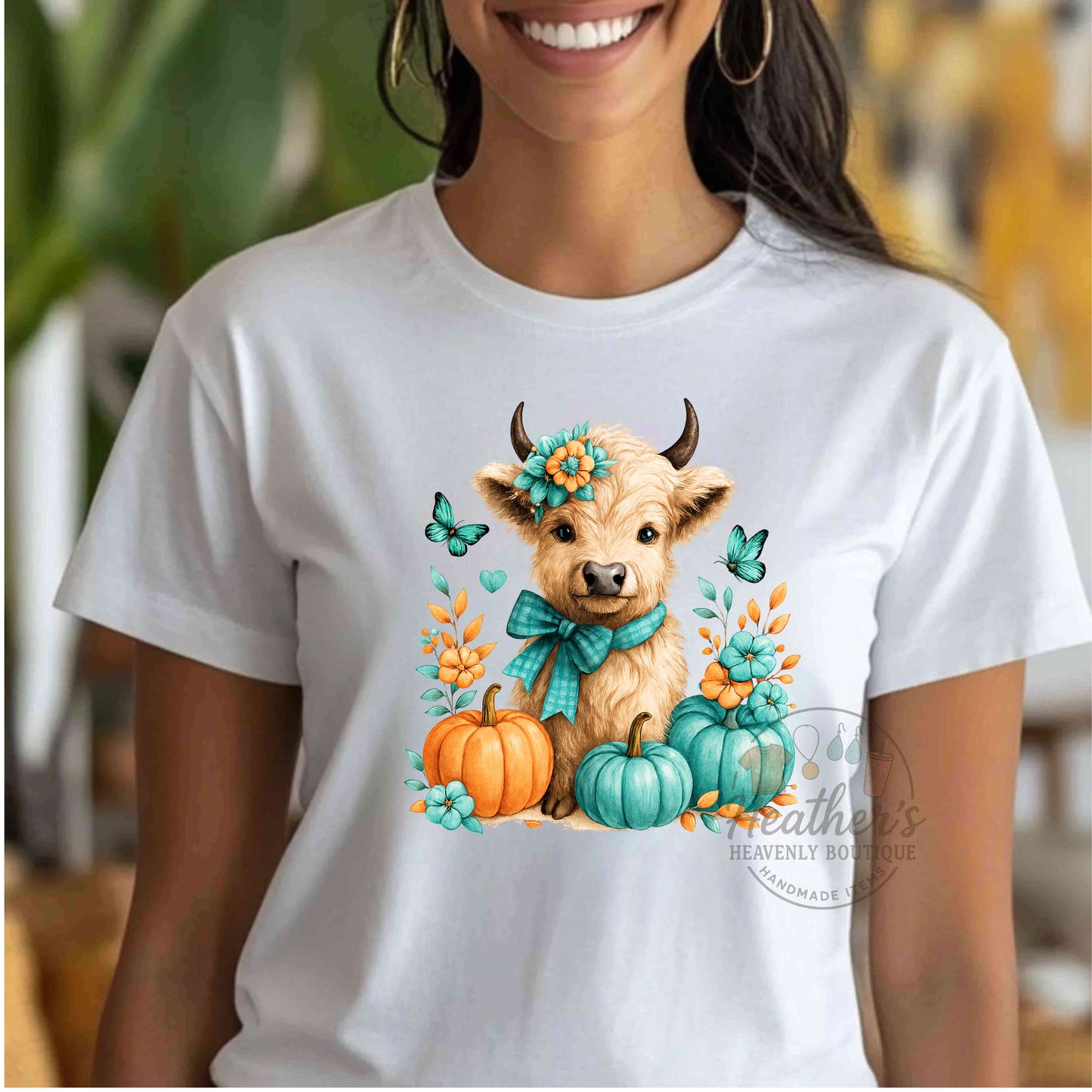 White t-shirt with a cow and pumpkins design worn by a person indoors.