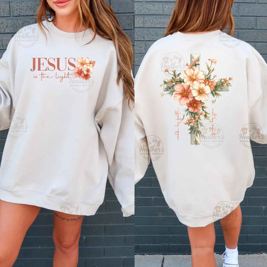 White sweatshirt with 'Jesus is the light' text and floral design on a gray brick wall background.
