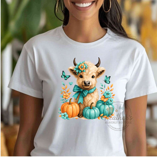 White t-shirt with a cow and pumpkins design worn by a person indoors.